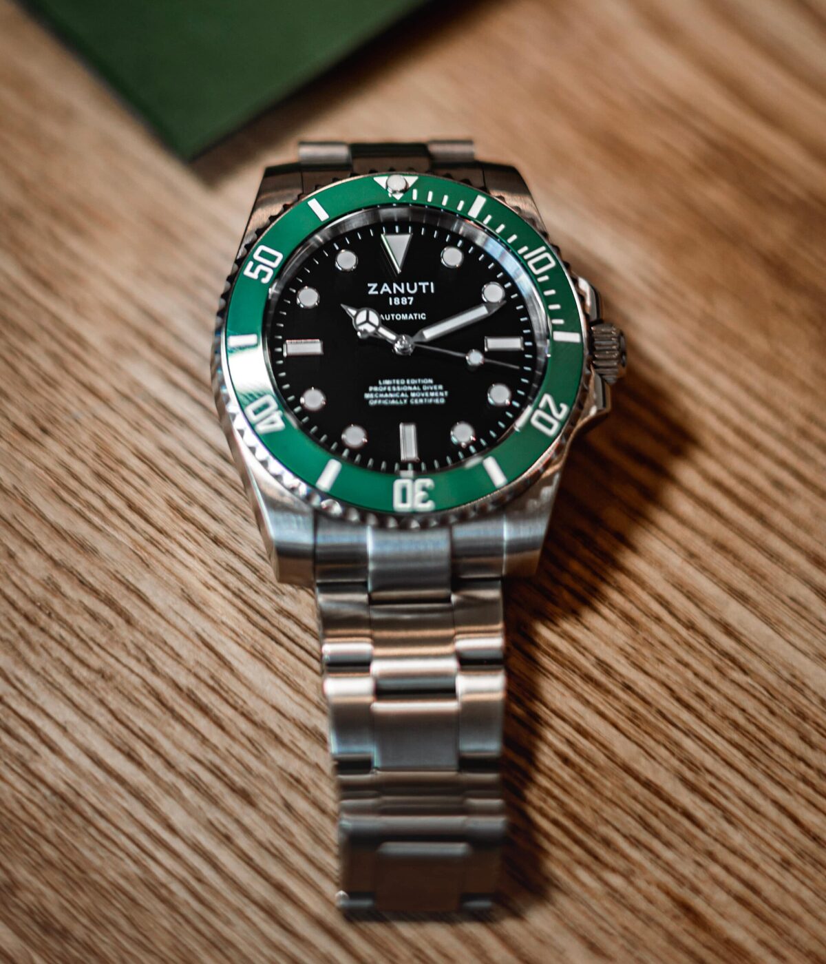 A stainless steel automatic dive watch with a green bezel lying on a wooden table