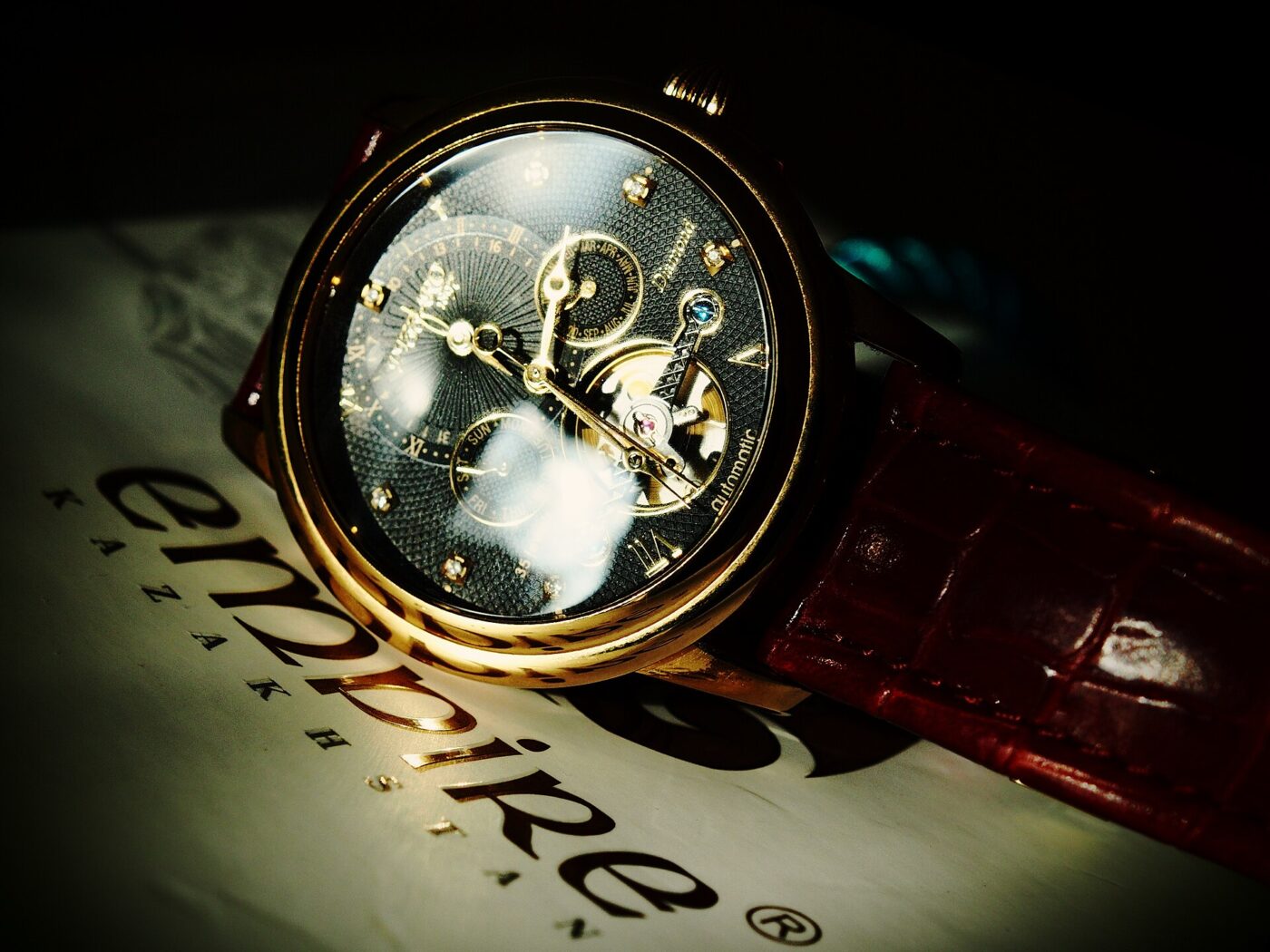 A gold-toned mechanical wristwatch with an open-worked dial and a brown leather strap