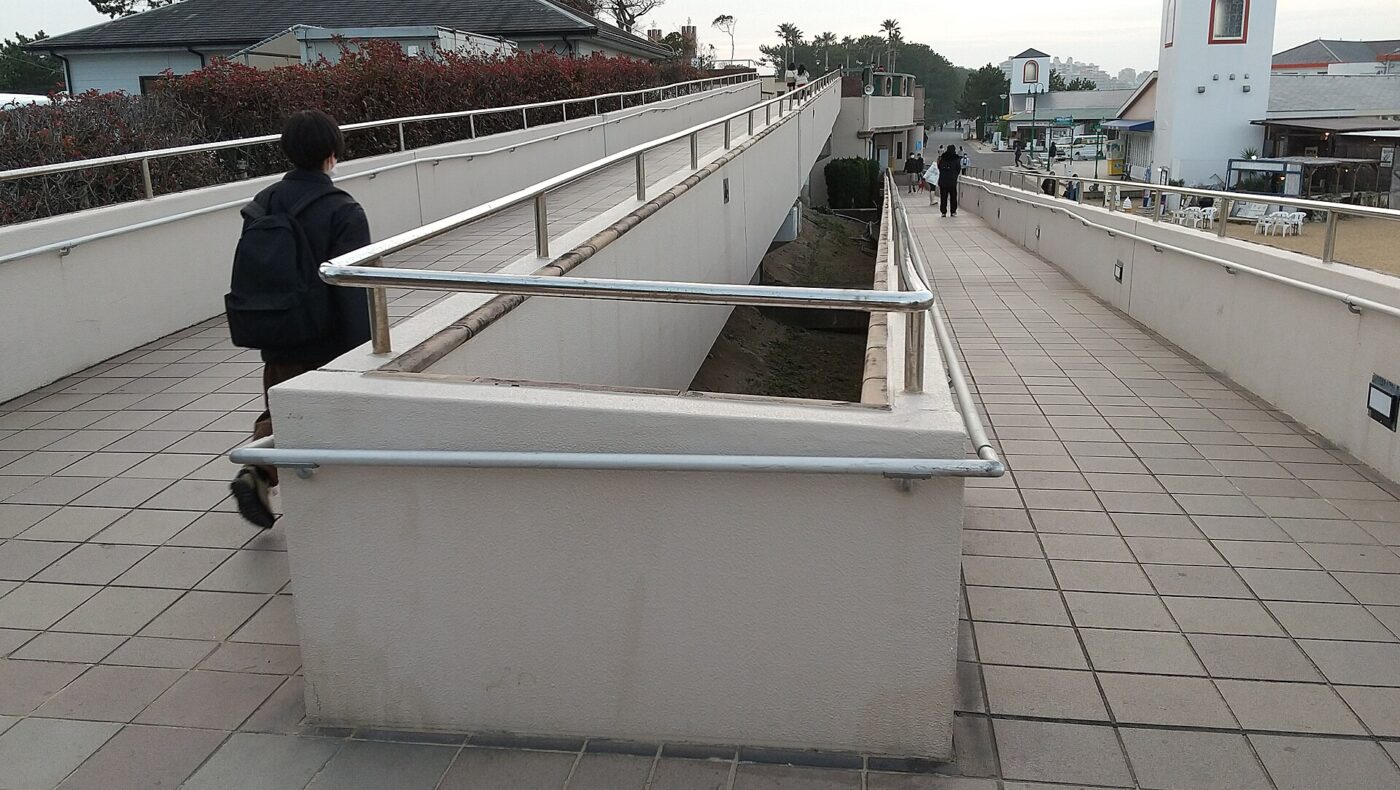 A switchback ramp with steel handrails climbs between a tiled deck and a lower walkway.