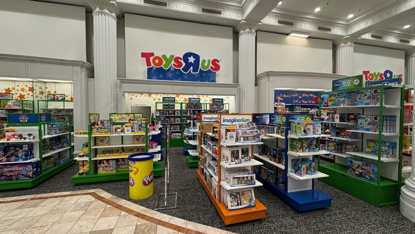 A Toys R Us toy department inside a department store, with rows of colorful shelves stocked with boxed toys