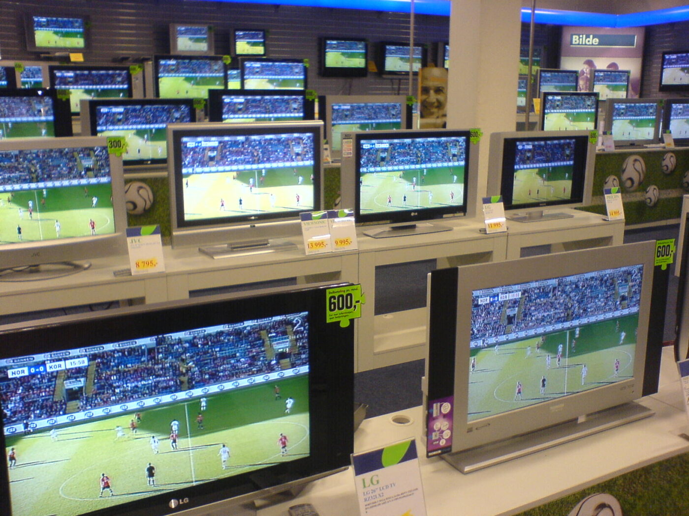 Flat-screen televisions lined up on store shelves with price cards, all showing the same soccer match