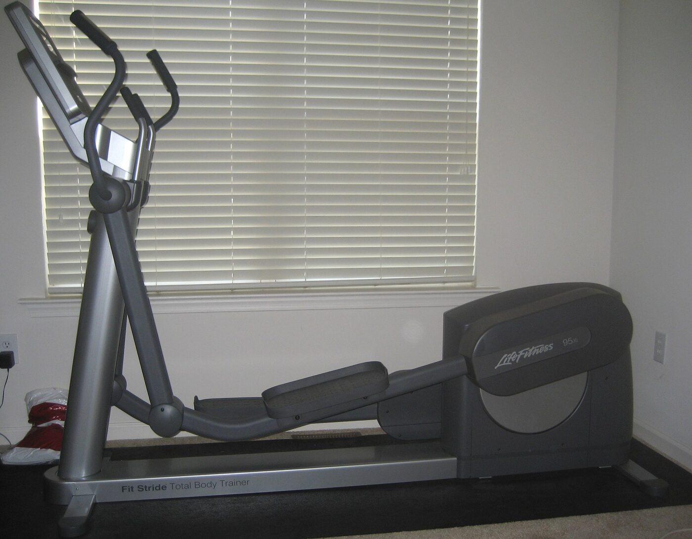 A full-size elliptical cross-trainer standing on a mat in a room beside a shaded window.