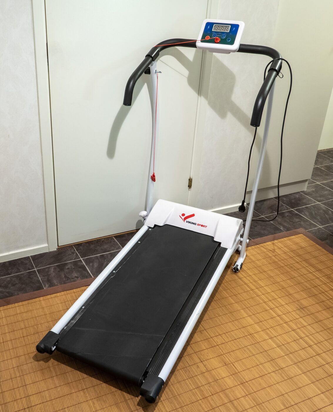 A compact folding treadmill with a small console, standing on the floor of a room.