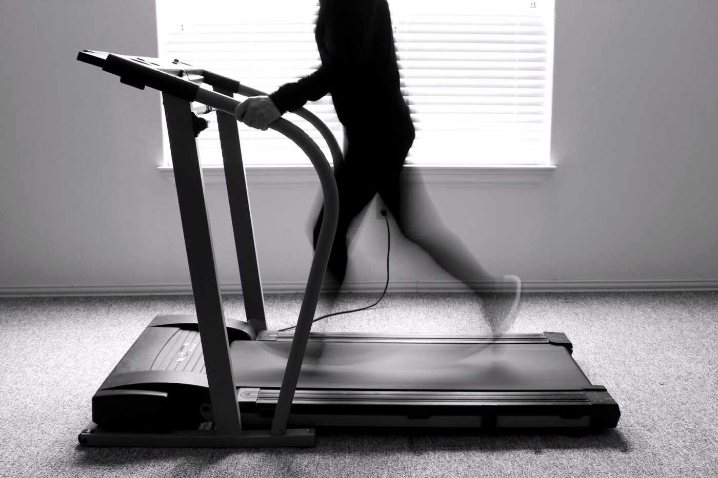 A folding home treadmill beside a bright window, with someone walking on the belt.