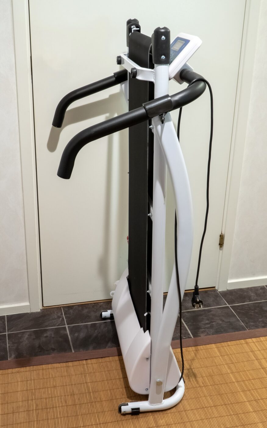 A folding treadmill stood upright on a tiled floor with its deck raised for storage.