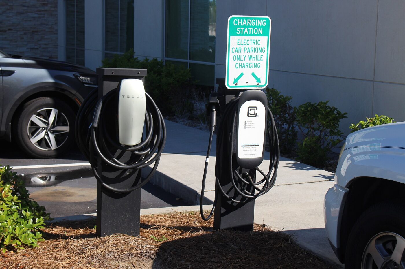 Two electric vehicle chargers beside a sign reserving the parking space for cars while charging