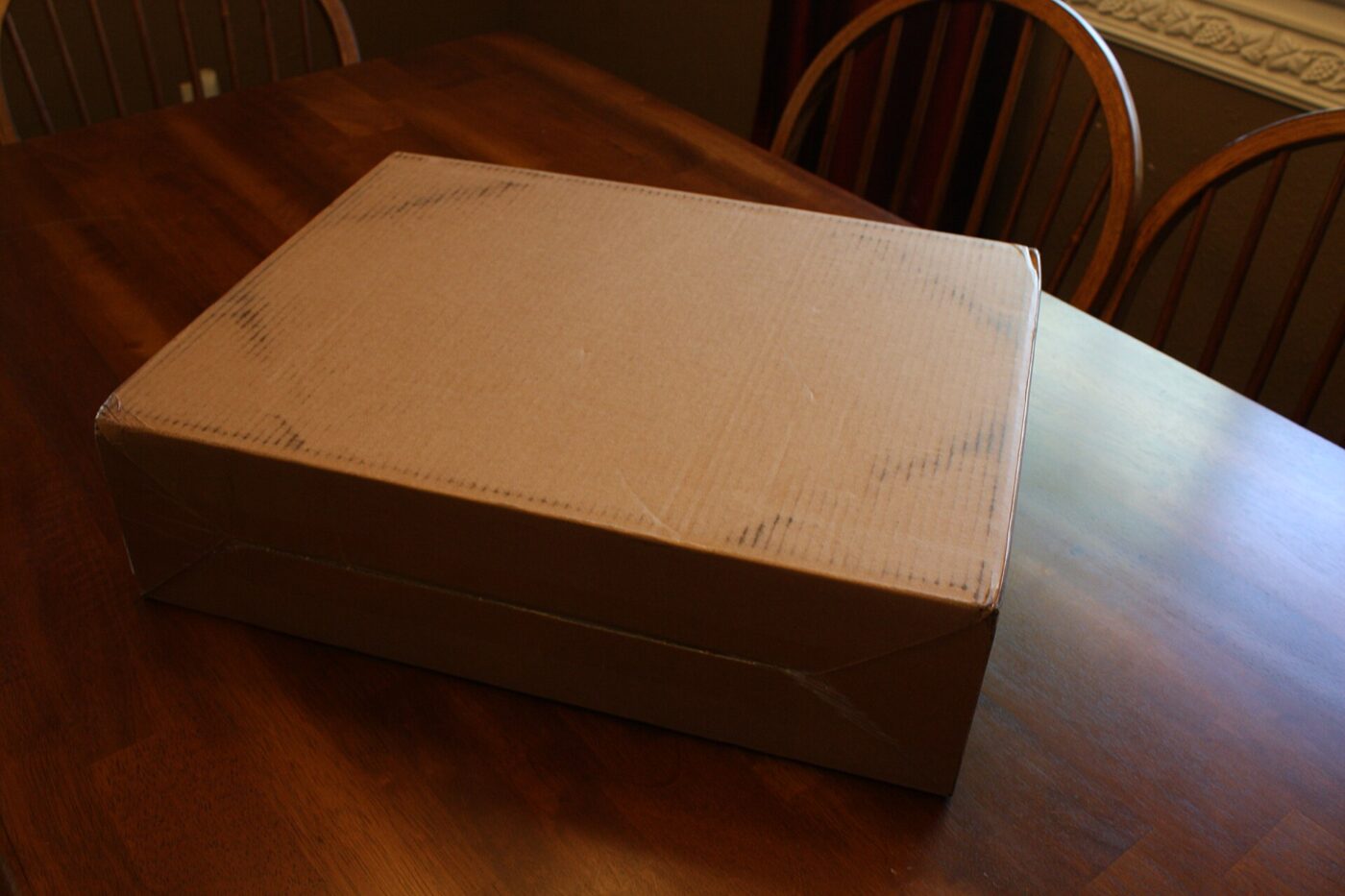 A taped, closed cardboard box sitting on a wooden dining table
