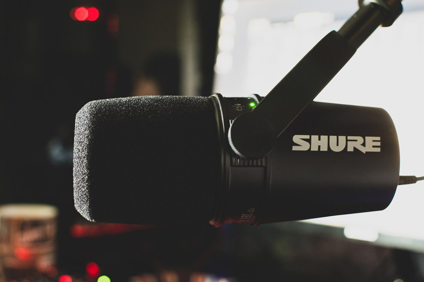 A Shure podcast microphone with a foam windscreen, mounted on a boom arm