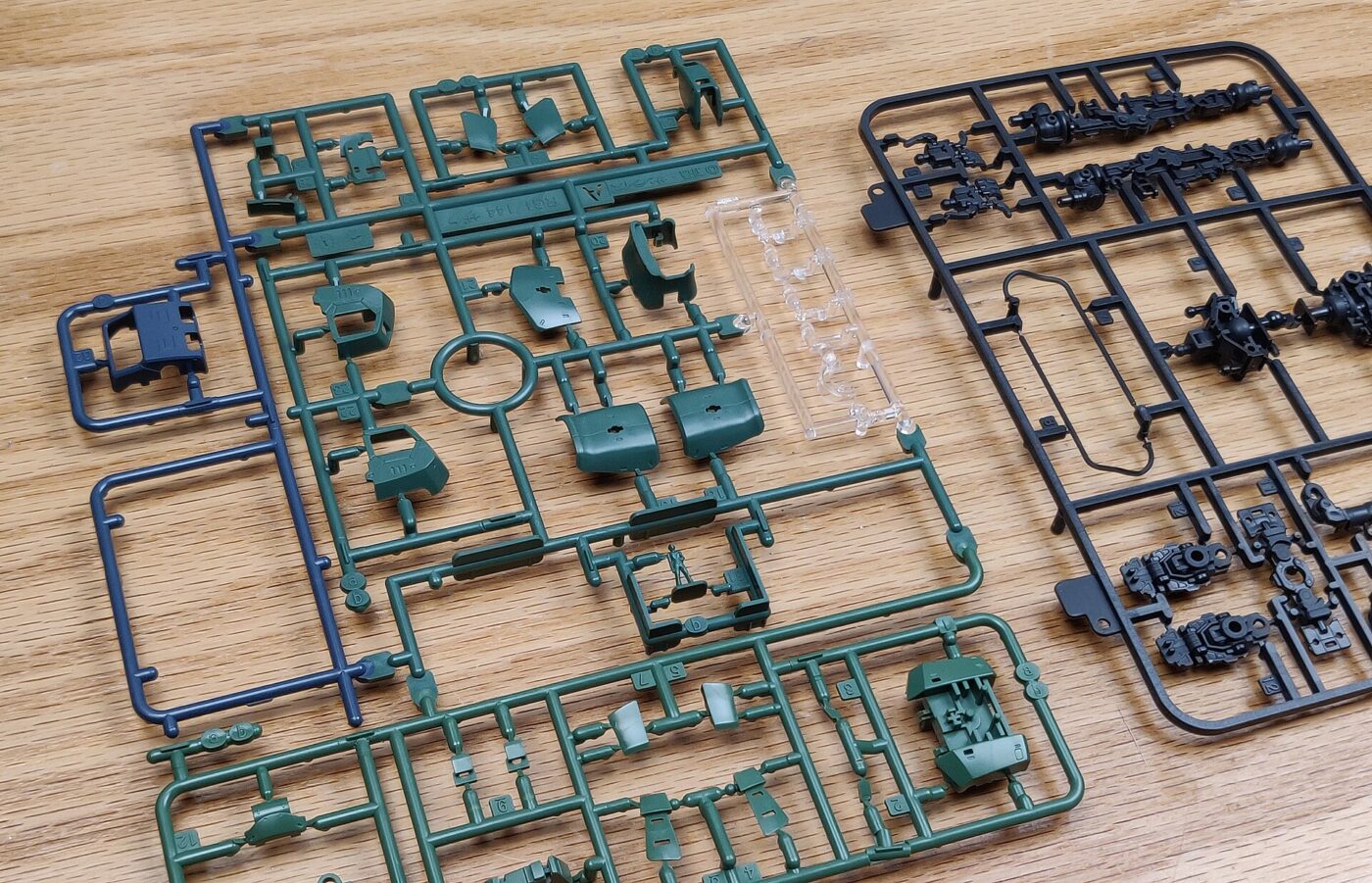 Unassembled plastic model kit parts still attached to green, blue and black sprues on a wooden table