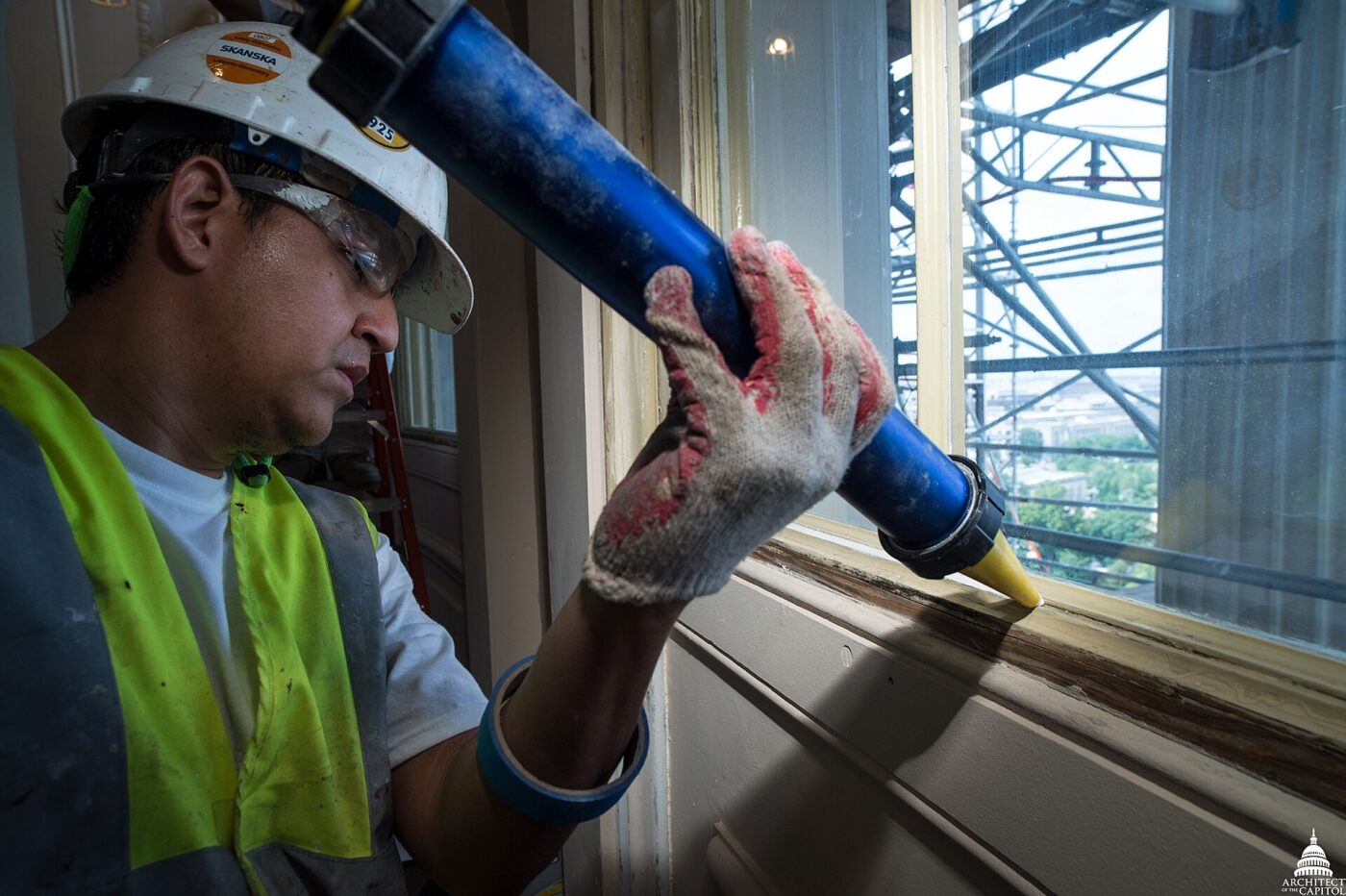 A worker in a hard hat runs a bead of caulk along a window frame.