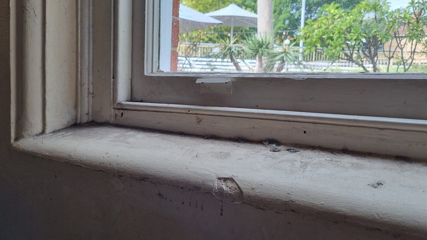 A close-up of an old window sash meeting a worn painted sill indoors.