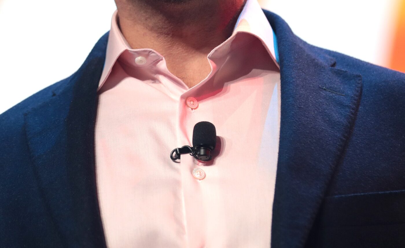 A small clip-on microphone attached to a pink dress shirt under a navy blazer