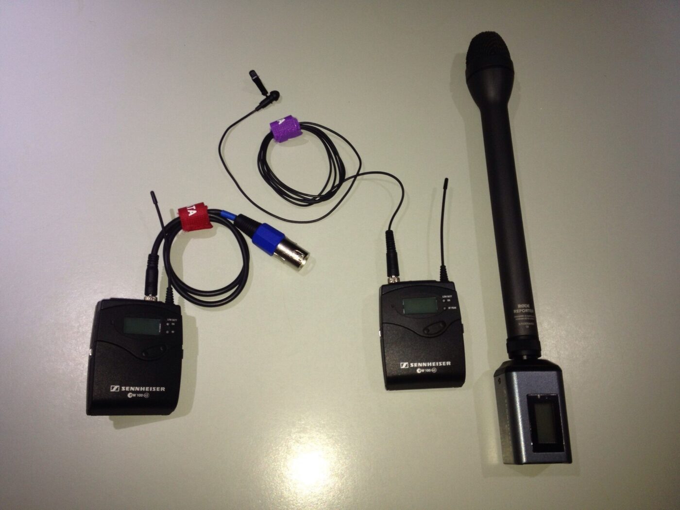 Two wireless belt-pack units laid out with a clip-on lavalier and a handheld reporter microphone.