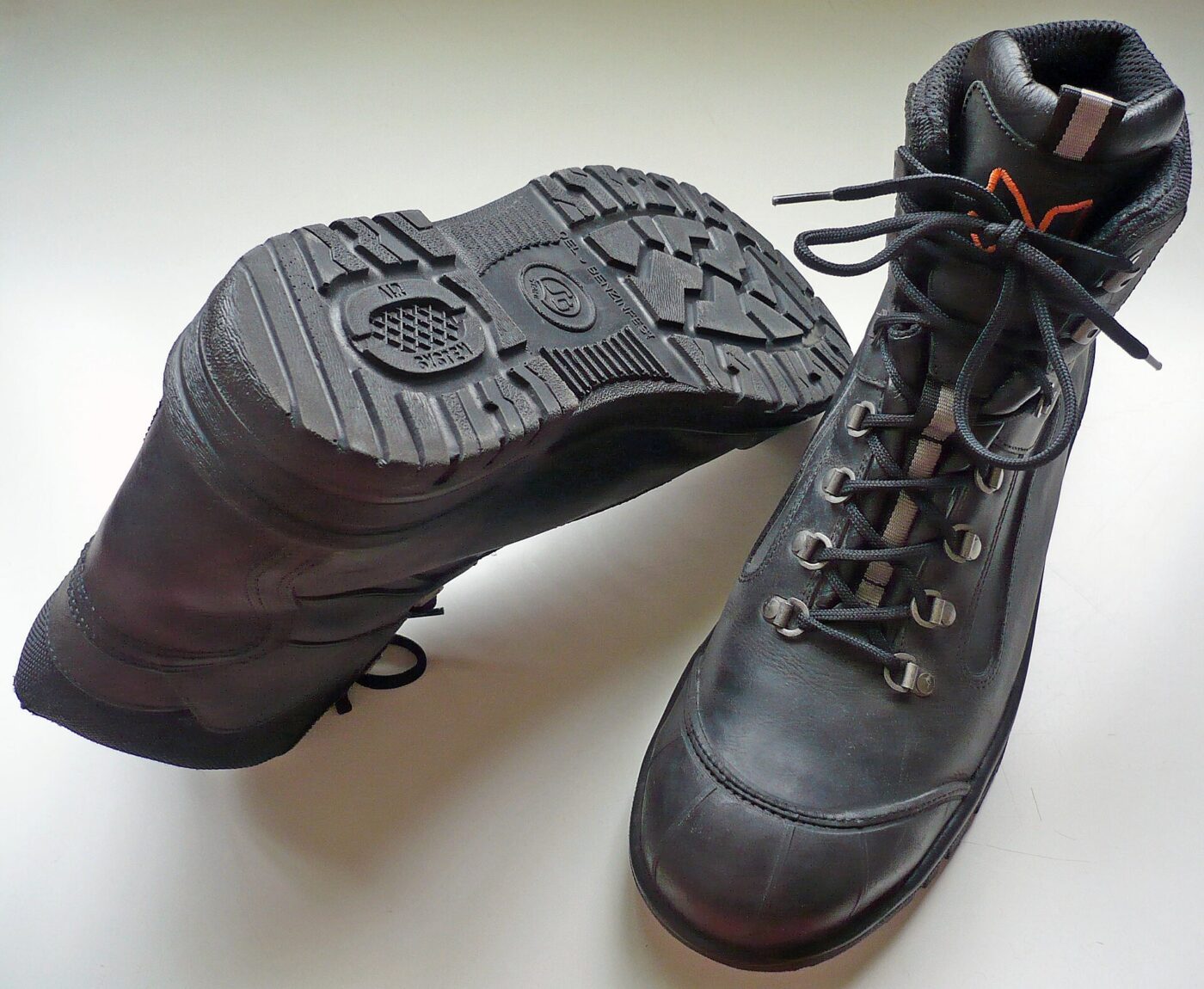 A pair of black leather safety boots, one turned to show its lugged sole