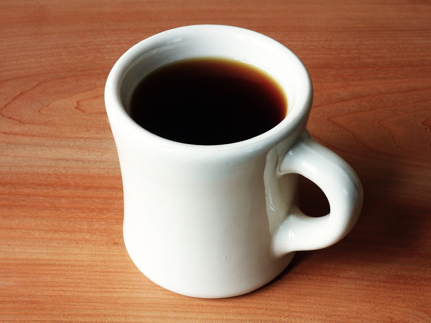 A plain white ceramic mug filled with black coffee on a wooden surface