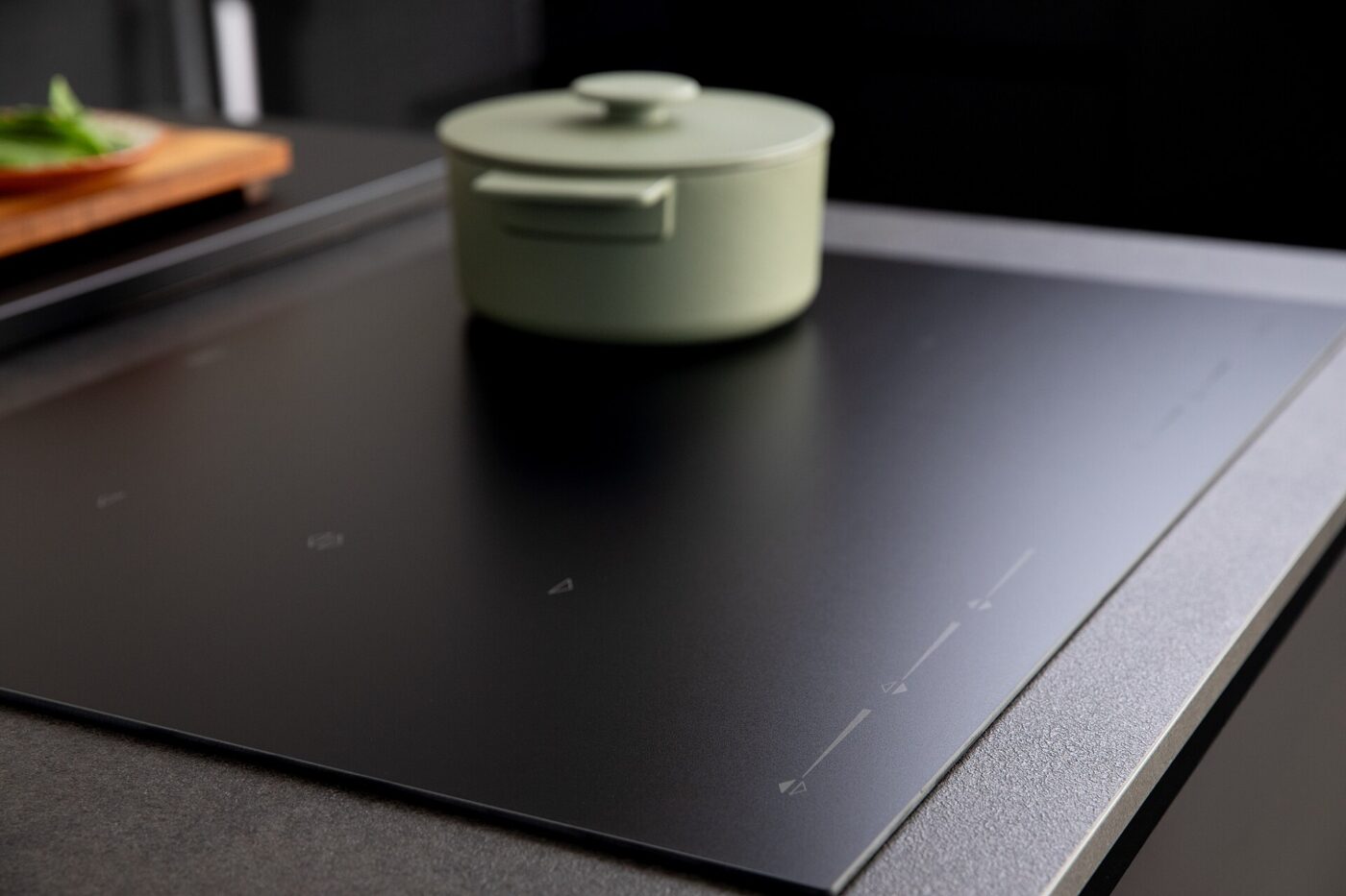 A lidded pot standing on a matte black glass cooktop with faint touch-control markings