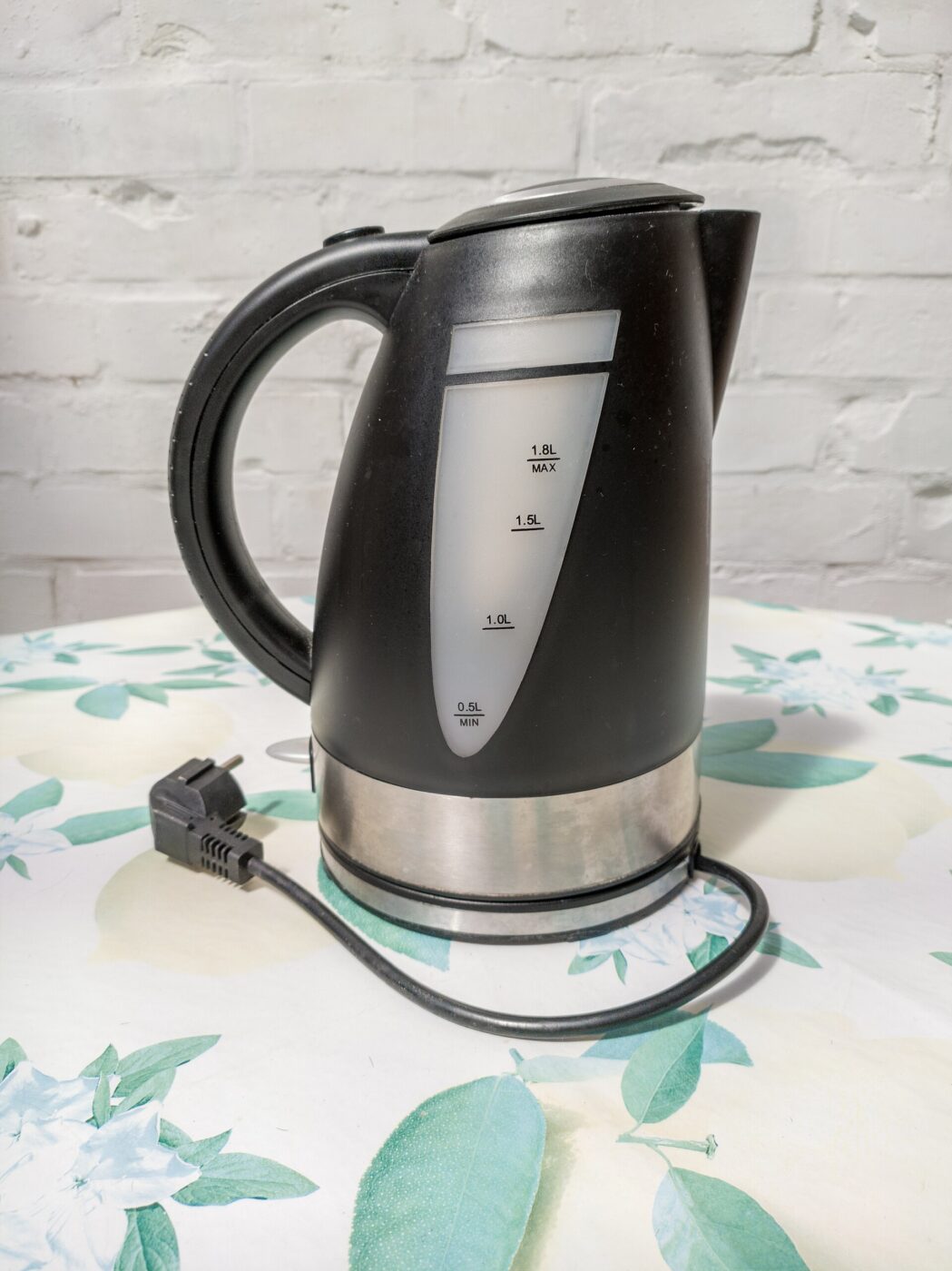 An electric kettle on a table, its handle joined to the body at top and base.