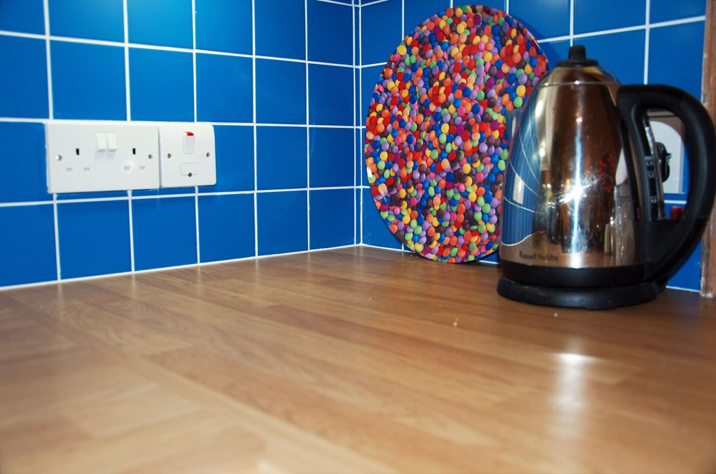 A stainless steel electric kettle on a wooden counter beside a blue tiled wall.