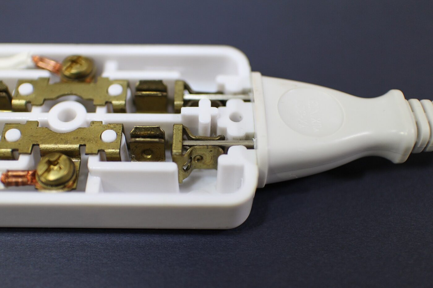 A power strip opened up, showing the brass contacts inside and the molded plug on its cord