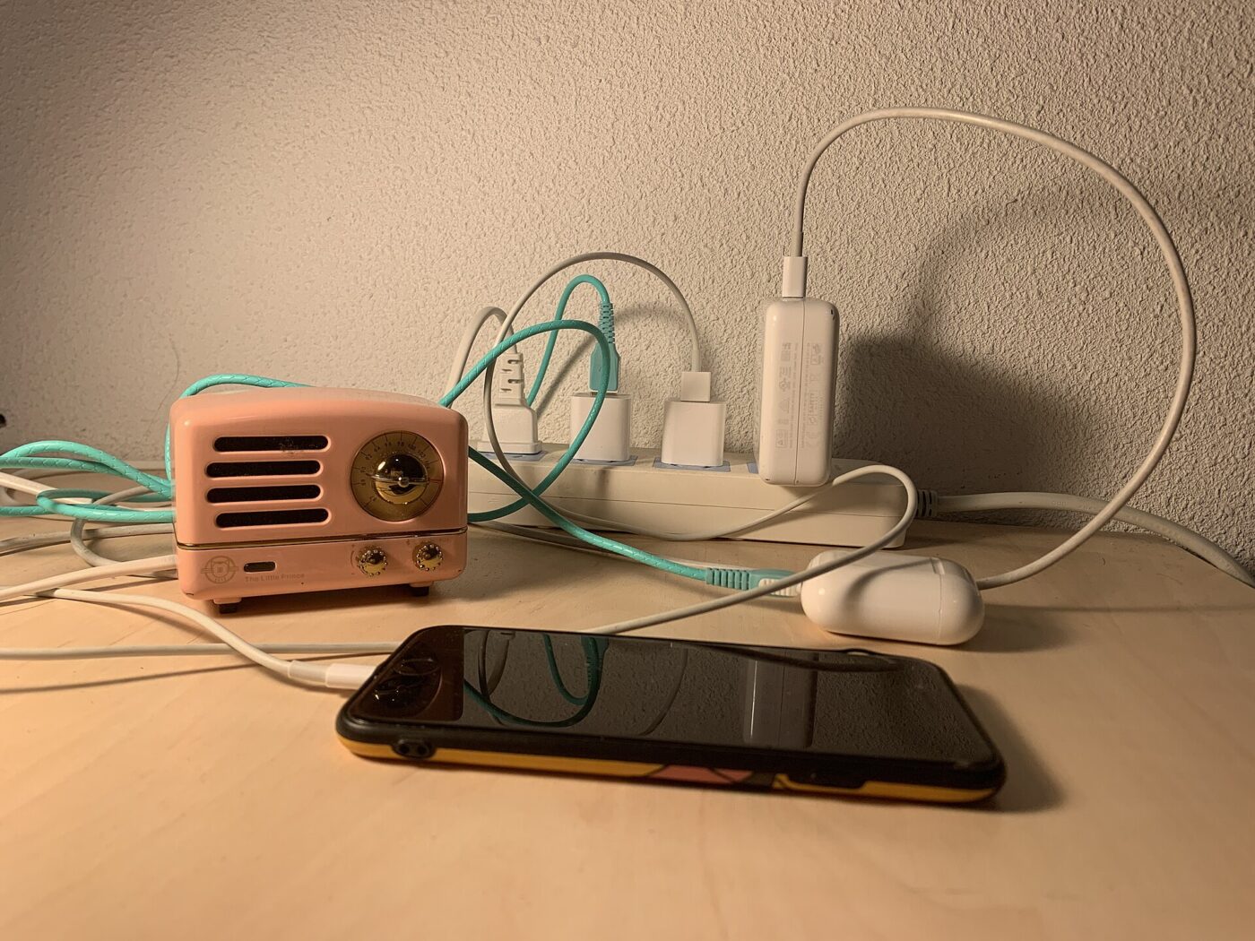 A power strip on a desk holding several phone chargers, beside earbuds and a small speaker