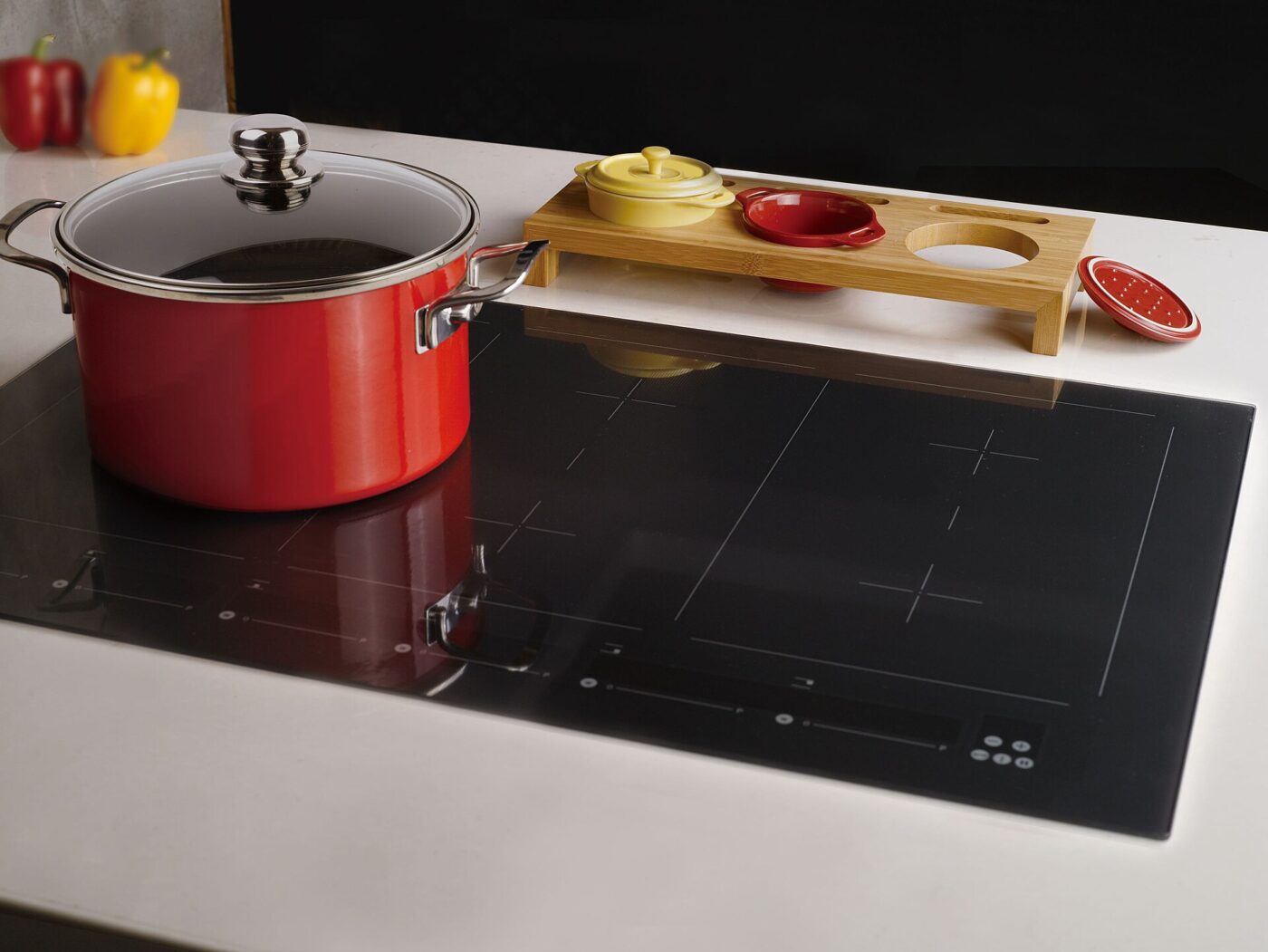 A red pot and a wooden serving board resting on a black glass cooktop