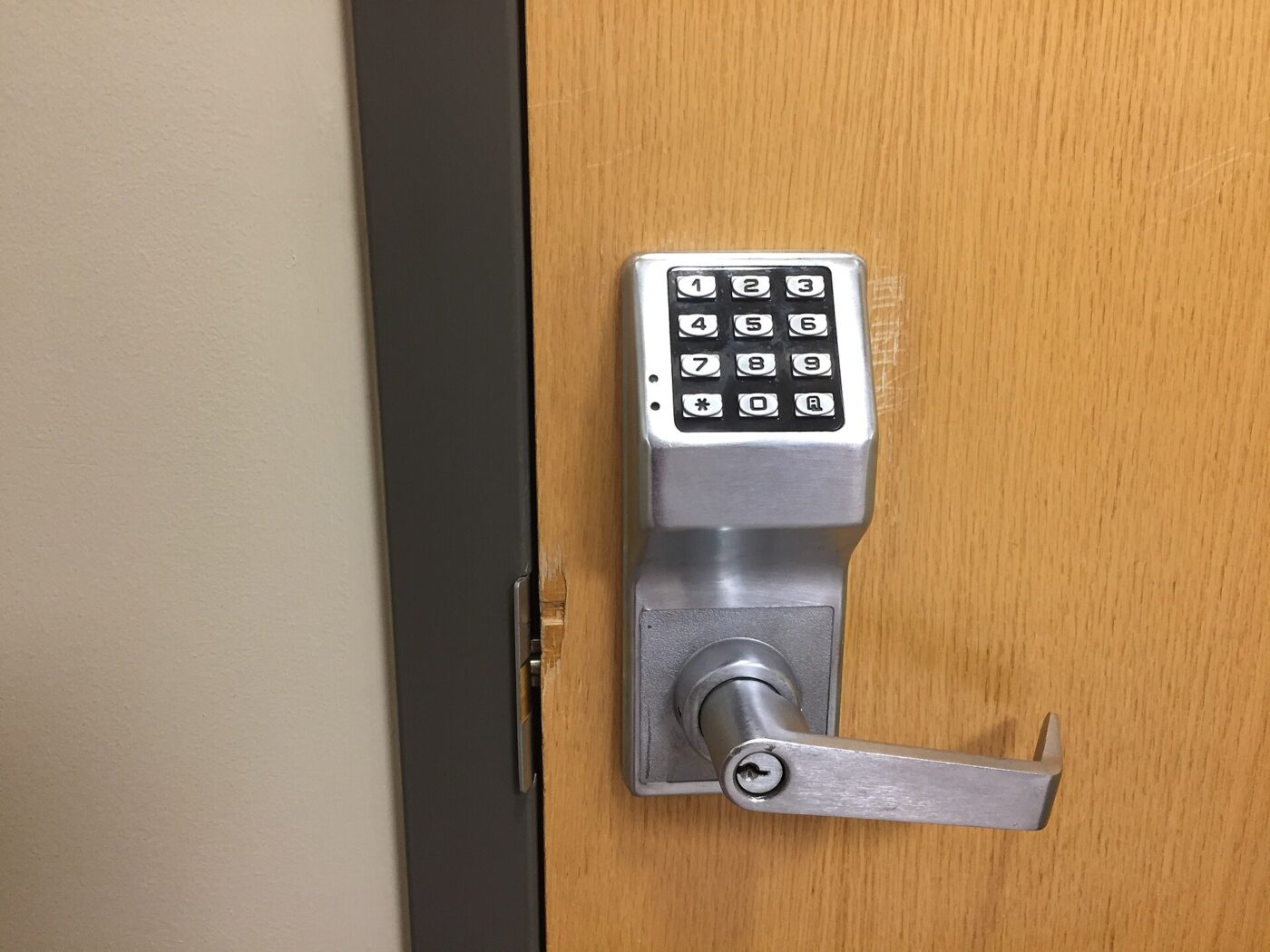 A stainless keypad entry lock with a lever handle mounted on a wooden door