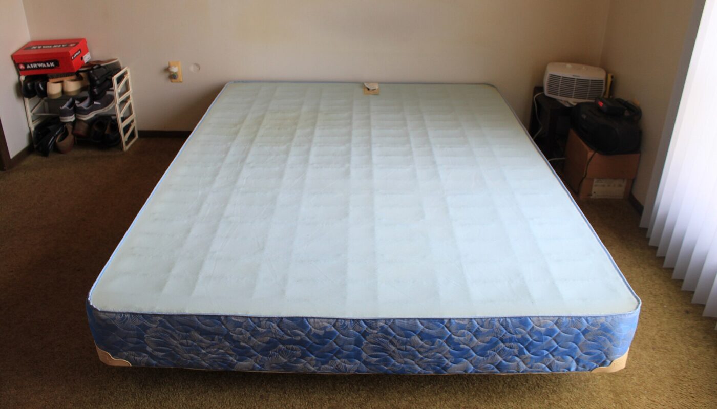 A quilted box spring resting on a metal bed frame in a bedroom, without a mattress.