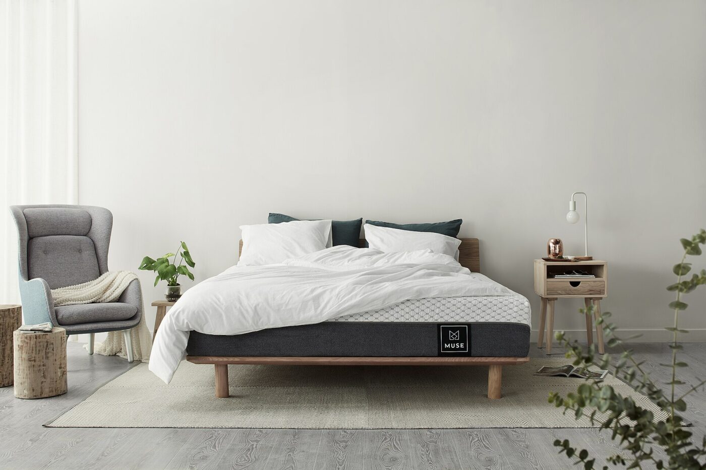 A bare mattress on a low wooden bed frame in a plain, brightly lit bedroom.