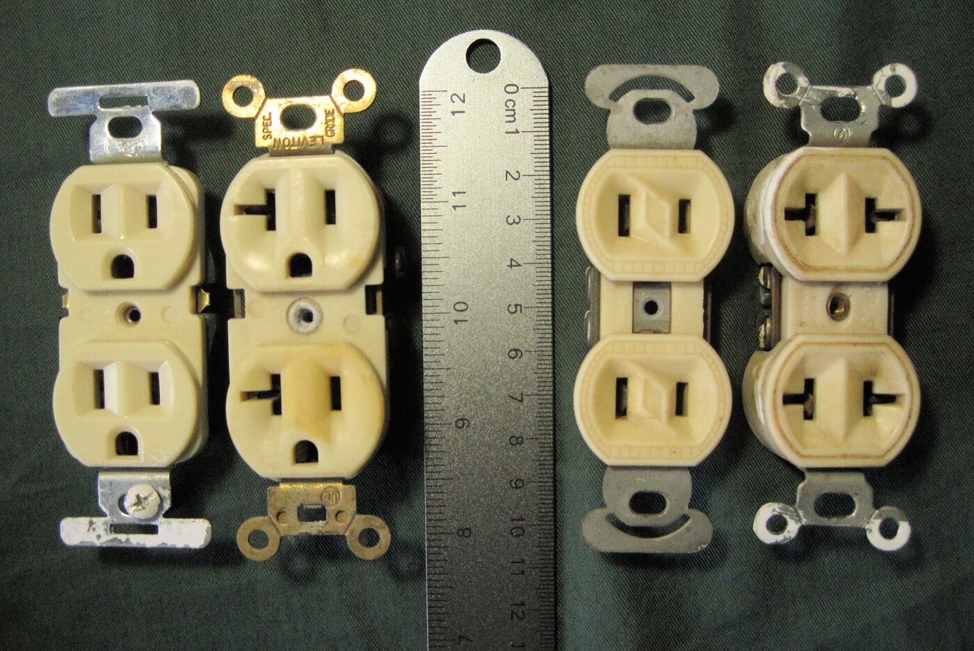Four standard North American duplex receptacles laid out beside a steel ruler for scale
