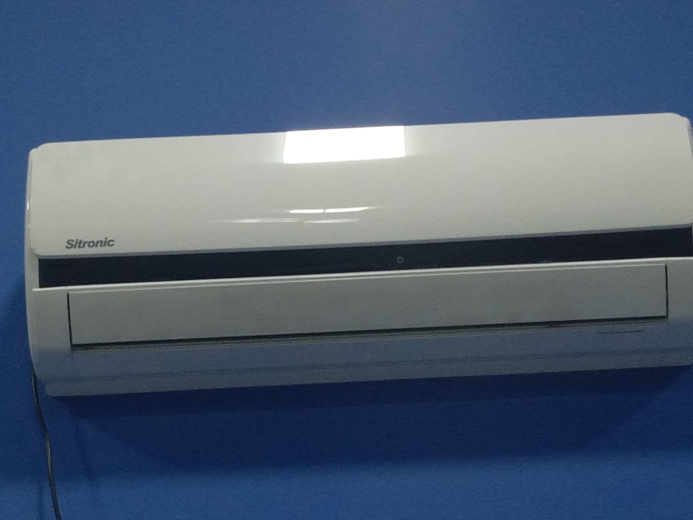 Close view of a white ductless indoor unit mounted high on a plain blue wall