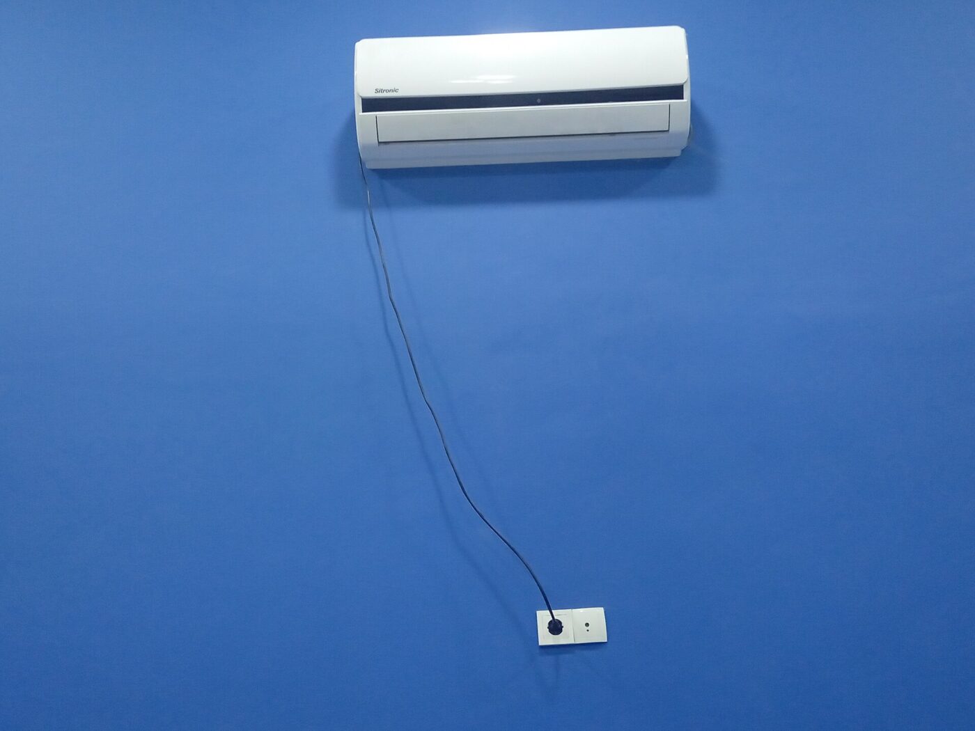 A white ductless indoor unit mounted on a blue wall, its cable run down to a socket