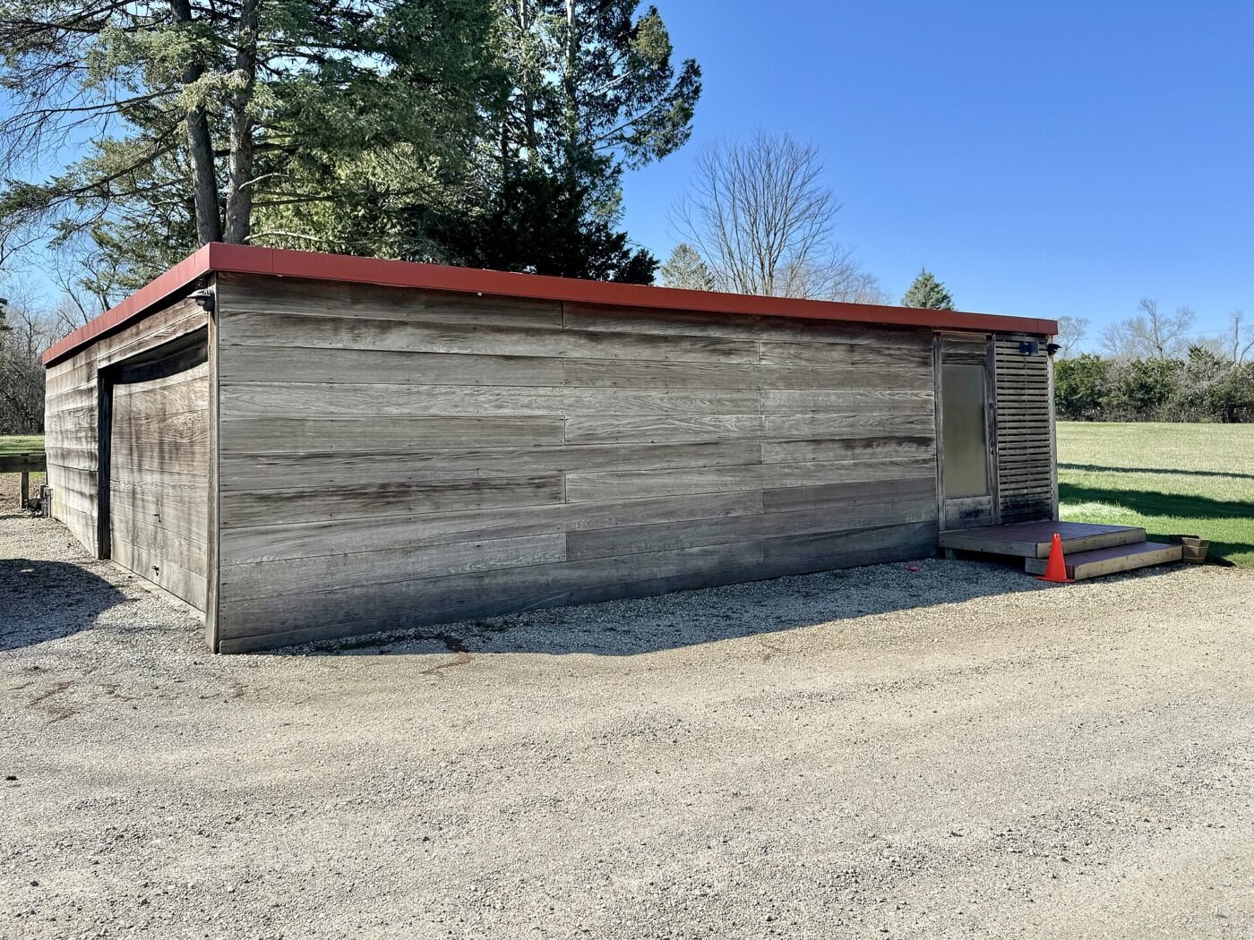 A long detached garage with weathered board siding beside a gravel drive