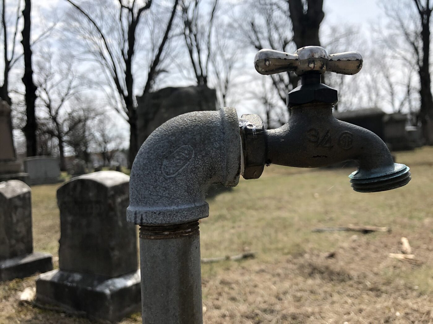 An outdoor wall faucet on a brick house with bare winter trees behind it