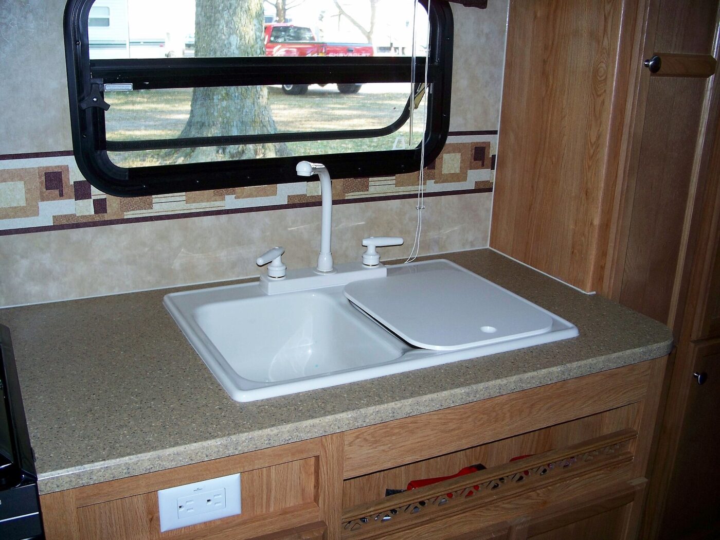 A camper galley with a double sink, oak cabinets and a duplex outlet below the counter