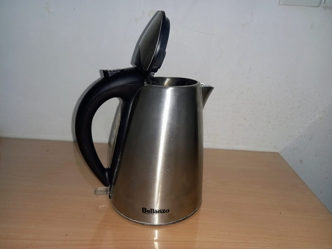 A stainless steel electric kettle with its lid open, standing on a wooden table.