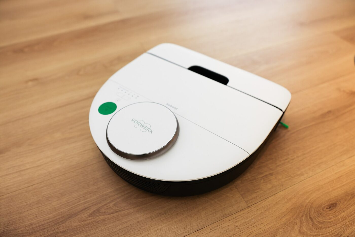A white robot vacuum cleaner on a wooden floor, seen from the front corner.