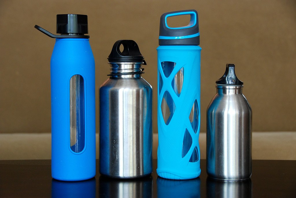 Four reusable drinking bottles in glass and stainless steel, lined up on a counter.
