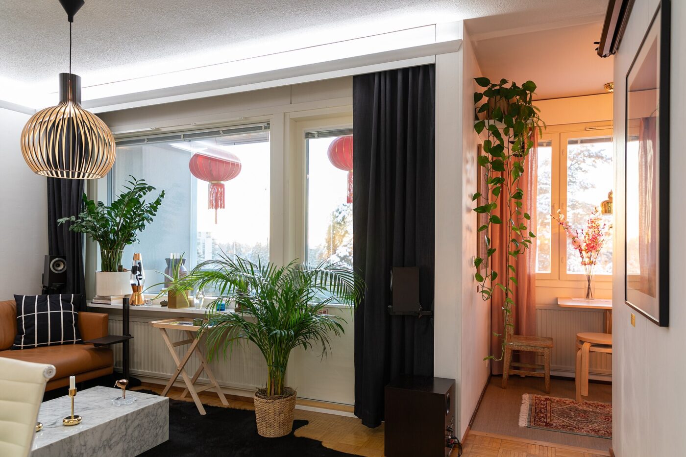 A bright one-room studio apartment with a dining table, houseplants and an open doorway beyond
