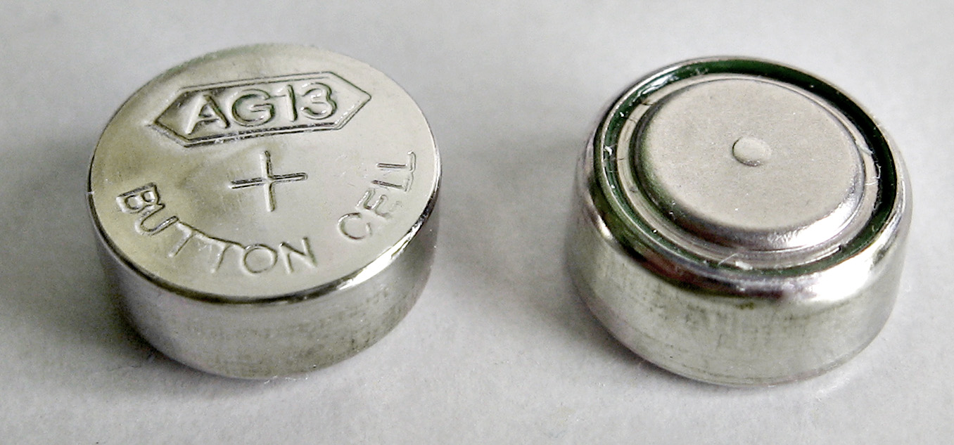 Two small button cell batteries, one standing on edge, on a plain background.