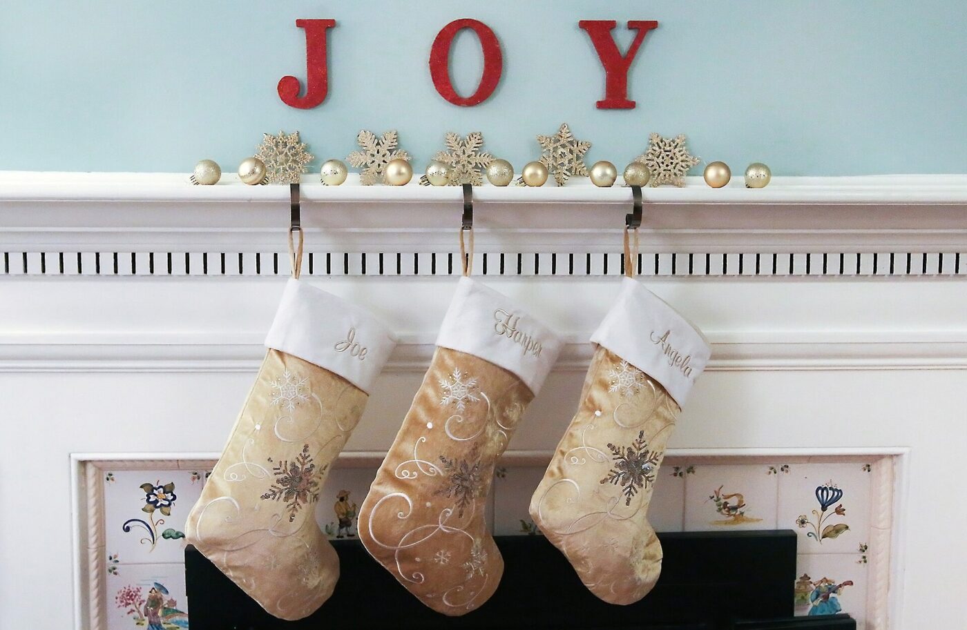 Christmas stockings hung from a white mantelpiece below red letters spelling joy.