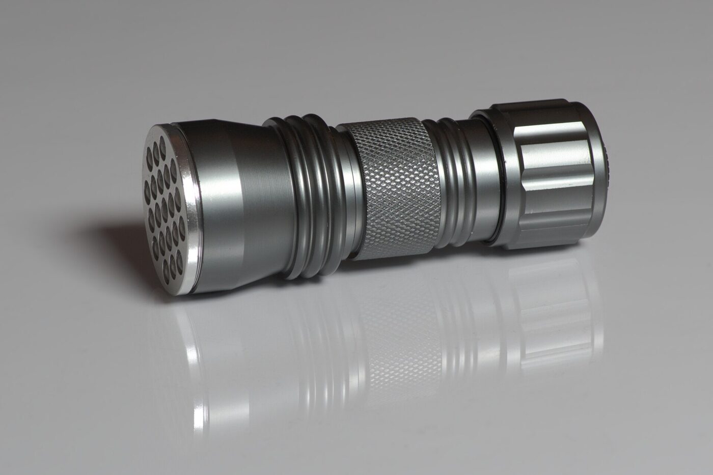 A compact aluminum flashlight with a ring of emitters in its head, on a grey surface.